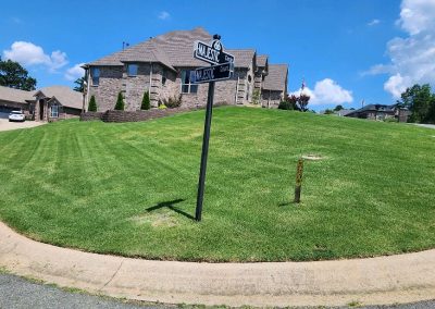 Well-manicured lawn with a house in the background, street sign for 