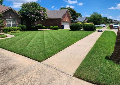 Well-maintained lawn with neatly striped grass and landscaped bushes outside a residential home in Central Arkansas, showcasing APEX Lawn Care services.