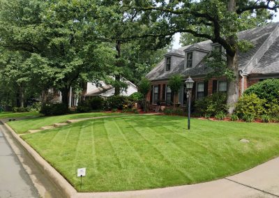 Lush green lawn with neatly striped grass, landscaped front yard of a suburban home in Central Arkansas, showcasing professional lawn care services by APEX Lawn Care.