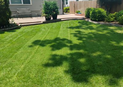 Lush green lawn with neatly striped grass, surrounded by landscaped garden beds and patio area, showcasing professional lawn care services by APEX Lawn Care in Central Arkansas.