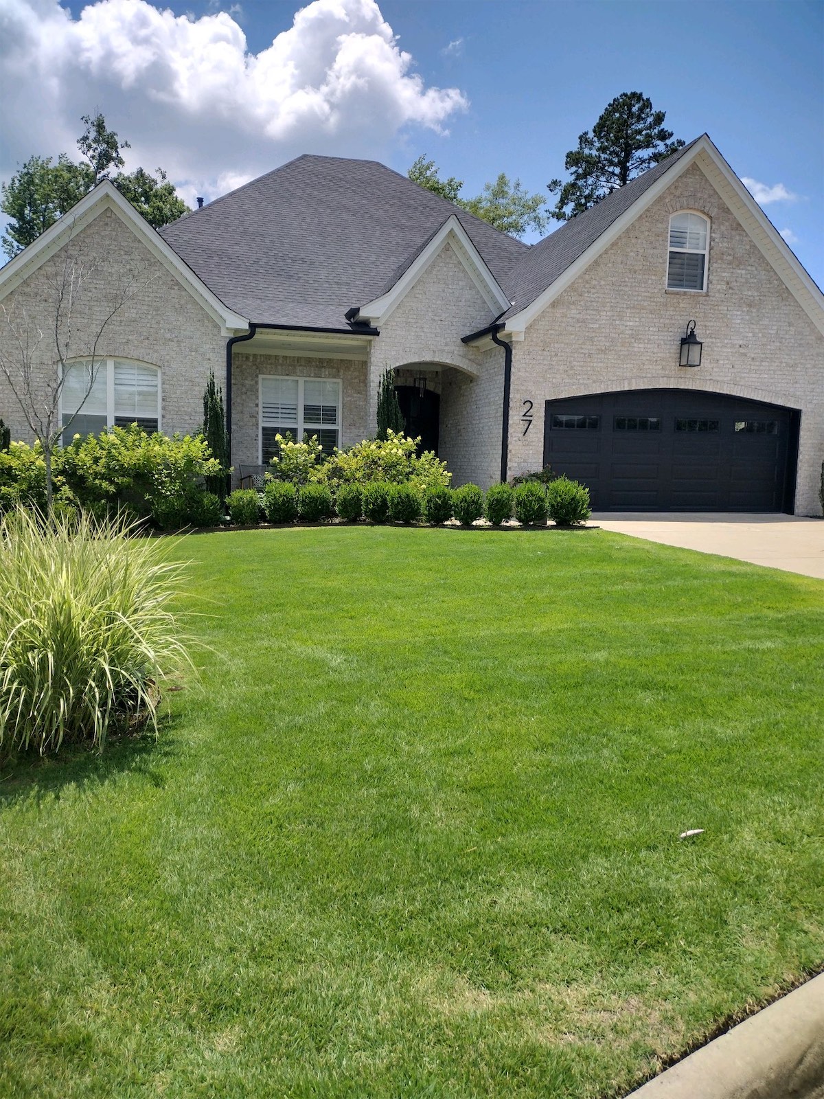 Beautifully manicured green lawn in front of a modern home with brick exterior, showcasing vibrant landscaping and clear blue sky, representing professional lawn care services in Little Rock.