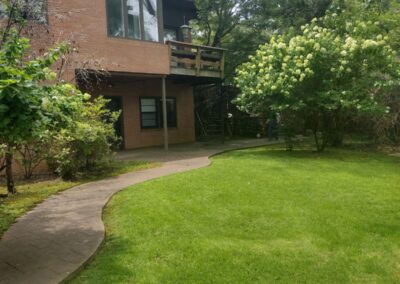 Lush green lawn with curved pathway leading to a residential building, showcasing APEX Lawn Care's landscaping services in Little Rock, Arkansas.