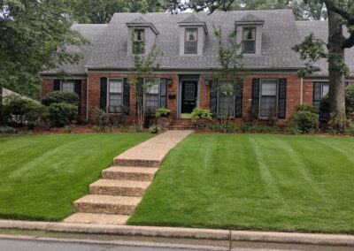 Lush green lawn with neatly trimmed grass and a stone pathway leading to a brick house, showcasing professional lawn care services by APEX Lawn Care in Little Rock, Arkansas.
