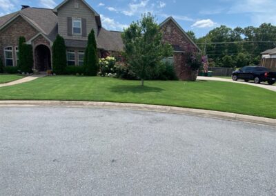 Lawn care service showcasing a well-maintained residential yard in Little Rock, Arkansas, featuring green grass, landscaped flower beds, and a brick house exterior.