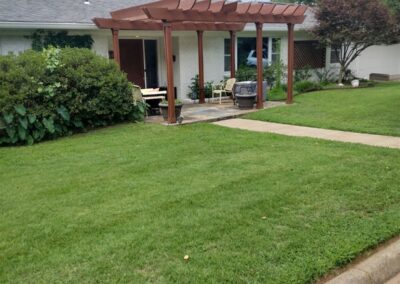 Lush green lawn with well-maintained landscaping and a wooden pergola in a residential yard, showcasing APEX Lawn Care's professional lawn care services in Little Rock, Arkansas.