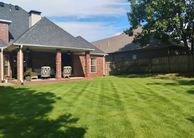 Lush green lawn with neatly striped grass and a brick patio featuring two outdoor chairs, showcasing APEX Lawn Care's professional lawn care services in Central Arkansas.