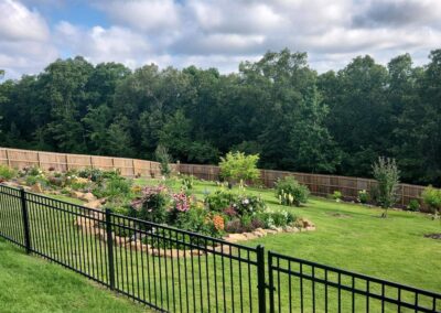 A well-maintained backyard garden with a variety of plants and flowers, bordered by a wooden fence and a metal railing. If the image does not contain an actual employee, then use the correct generated wording. - Little Rock Lawn Care and Mowing Services by Apex Lawn Care