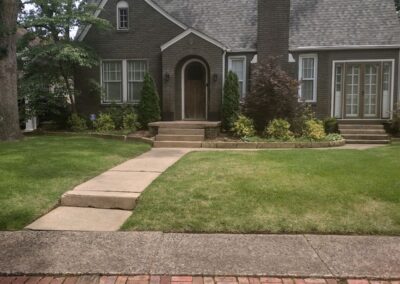 A brick pathway leading to a traditional house with a gabled roof and arched front door with a perfectly manicured lawn. - Little Rock Lawn Care and Mowing Services by Apex Lawn Care
