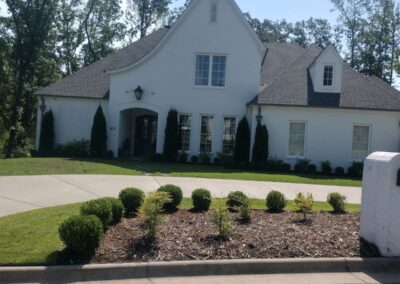 White two-story suburban house with a well-manicured lawn and shrubbery under a clear sky. - Little Rock Lawn Care and Mowing Services by Apex Lawn Care