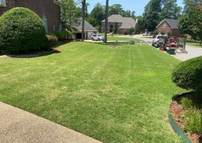 A well-manicured lawn in front of suburban houses on a sunny day with employees working. - Little Rock Lawn Care and Mowing Services by Apex Lawn Care