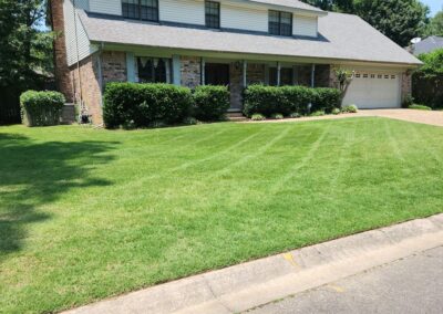 A neatly trimmed lawn in front of a two-story brick house with a double garage on a sunny day. - Little Rock Lawn Care and Mowing Services by Apex Lawn Care
