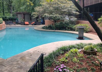 A serene outdoor swimming pool area surrounded by lush greenery and trees, featuring a lounging area and a fence. This space is ideal for anyone seeking relaxation or an outdoor meeting location. - Little Rock Lawn Care and Mowing Services by Apex Lawn Care