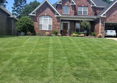 An employee brick suburban house with a well-manicured lawn and a partly open garage under a clear blue sky. - Little Rock Lawn Care and Mowing Services by Apex Lawn Care