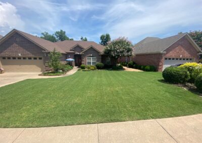 A single-story residential home with a well-maintained lawn and blooming trees under a clear blue sky is perfect for an employee. - Little Rock Lawn Care and Mowing Services by Apex Lawn Care