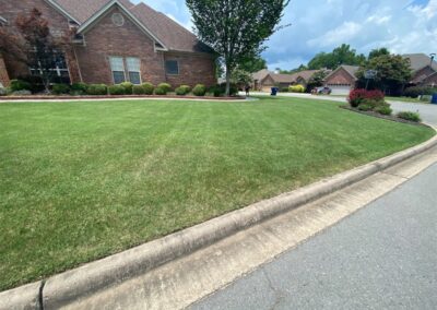 A well-manicured front lawn of a brick house with a curved sidewalk and clear skies. - Little Rock Lawn Care and Mowing Services by Apex Lawn Care