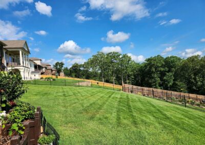 An employee meticulously maintains a lawn next to a residential area in the Little Rock Metro Area, all secured with a metal fence under a clear blue sky. - Little Rock Lawn Care and Mowing Services by Apex Lawn Care