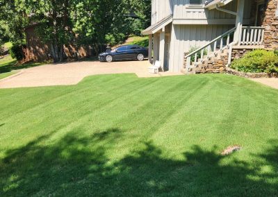 Lush green lawn with neatly striped grass, adjacent to a house and driveway, showcasing professional lawn care services by APEX Lawn Care in Central Arkansas.