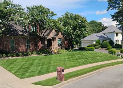Lush, well-manicured lawn in front of a brick home with neatly trimmed hedges and trees, showcasing professional lawn care services by APEX Lawn Care in Central Arkansas.