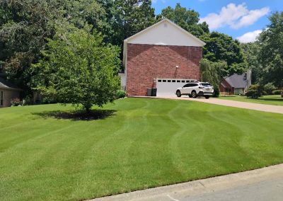 Well-maintained green lawn with neatly striped grass, featuring a brick house and a parked white SUV in Central Arkansas.