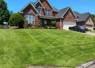 Well-maintained green lawn in front of a brick house, showcasing professional lawn care services by APEX Lawn Care in Central Arkansas.